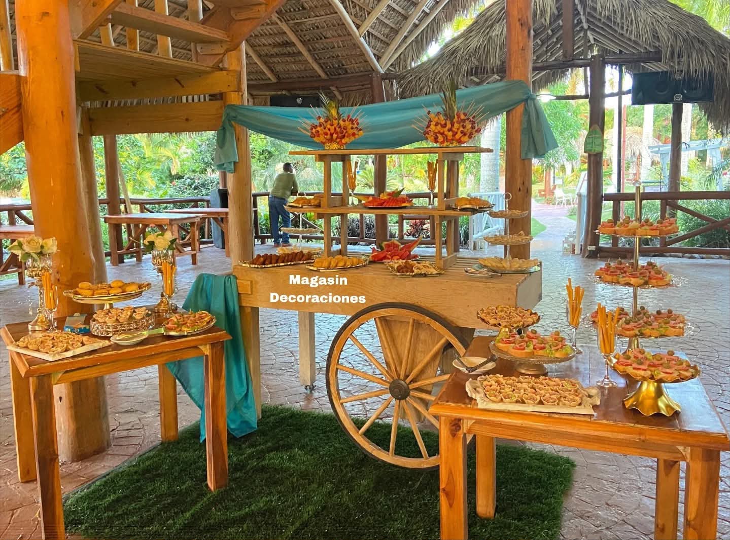 Carreta de madera con picaderas, frutas y canapés bajo un ranchón, decorada con tela turquesa por Magasin Victoria