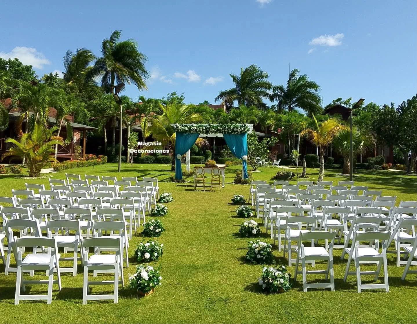 Ceremonia de boda en jardín con sillas blancas, pasillo de flores y altar con cortinas turquesa, en Higüey