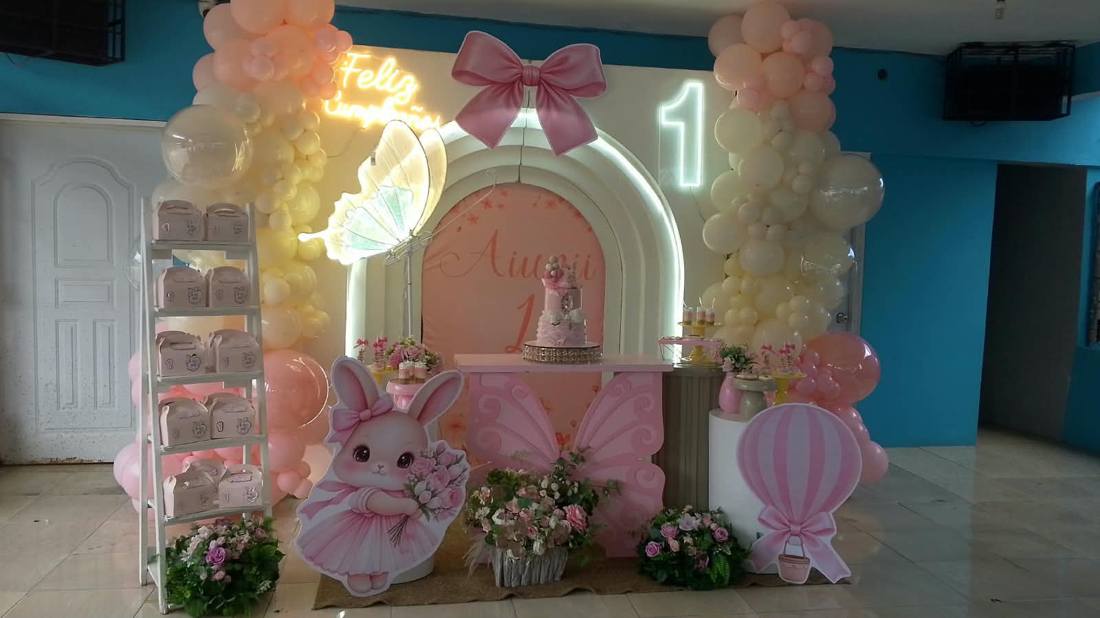 Decoración de primer cumpleaños rosa con neón 'Feliz Cumpleaños', mariposa luminosa, conejita y arco de globos por Magasin Victoria
