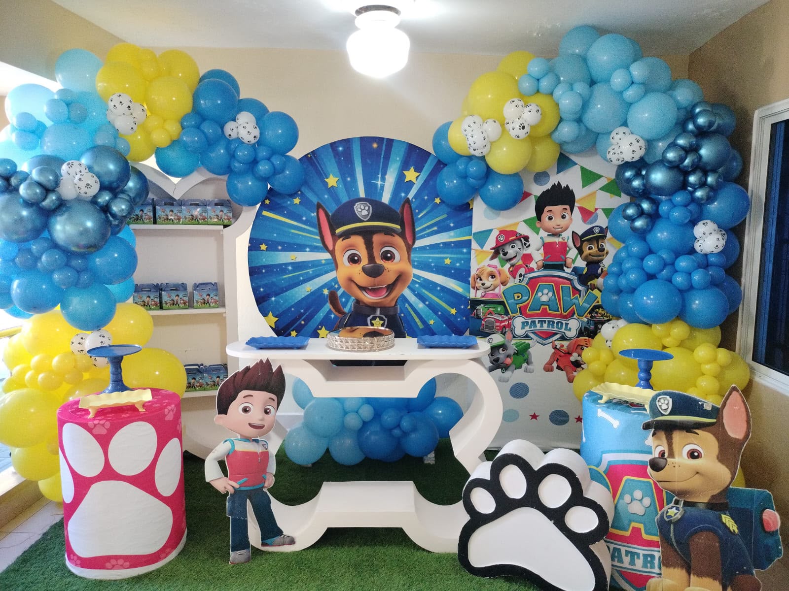 Cumpleaños infantil de Paw Patrol con arco de globos azules y amarillos, mesa en forma de hueso y figuras de Chase y Ryder