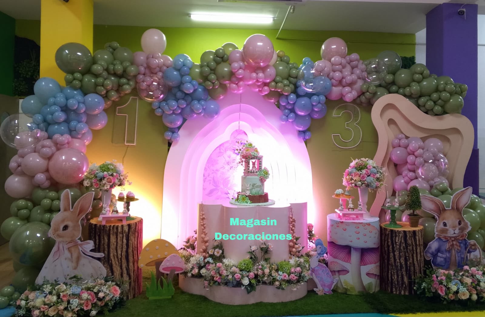 Montaje de cumpleaños temático de conejitos con globos rosa, verde y azul, hongos, troncos y flores, por Magasin Victoria en Higüey