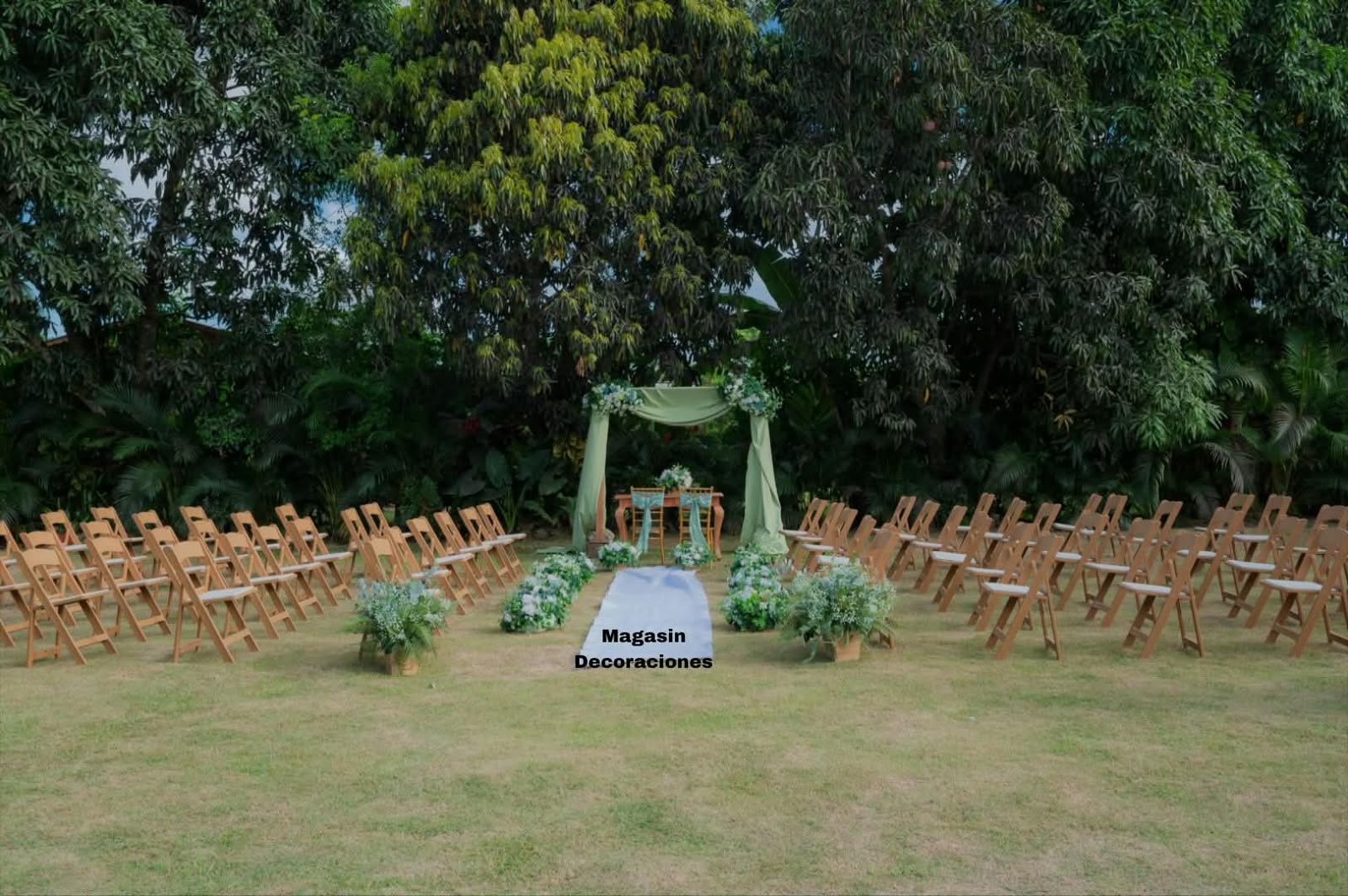 Ceremonia en jardín con sillas de madera, pasillo blanco, arreglos de flores y arco con telas verde salvia en Higüey