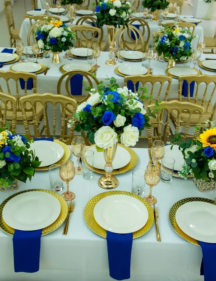 Fila de mesas decoradas por Magasin Victoria en salón blanco, centros florales azul y girasoles