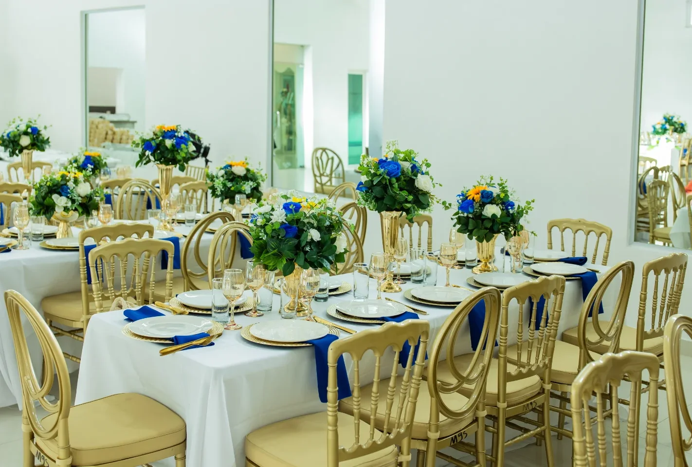 Mesas de boda montadas por Magasin Victoria junto a espejos de piso a techo, centros florales azul y blanco